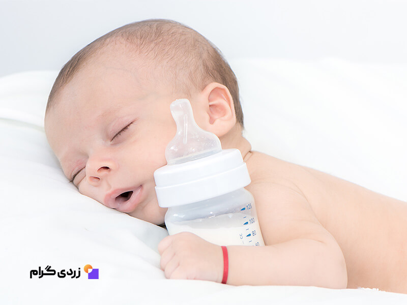 نوزاد خوابیده در حال بغل گرفتن شیشه شیر